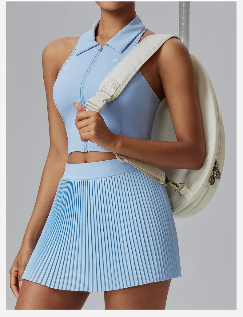 KiKis Women's Organ Pleated Tennis Skirt in light blue worn with a matching sleeveless zip-up top and white backpack