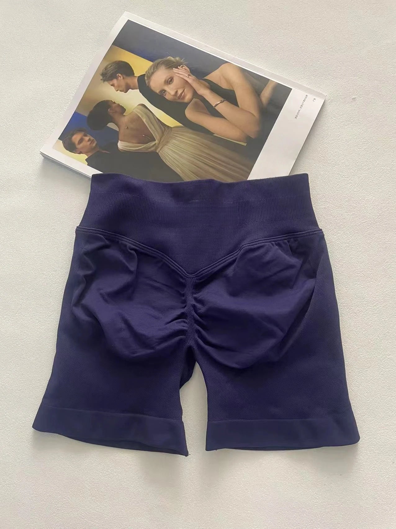 KiKis women's peach hip yoga shorts in dark purple laid flat on a white surface with a fashion magazine