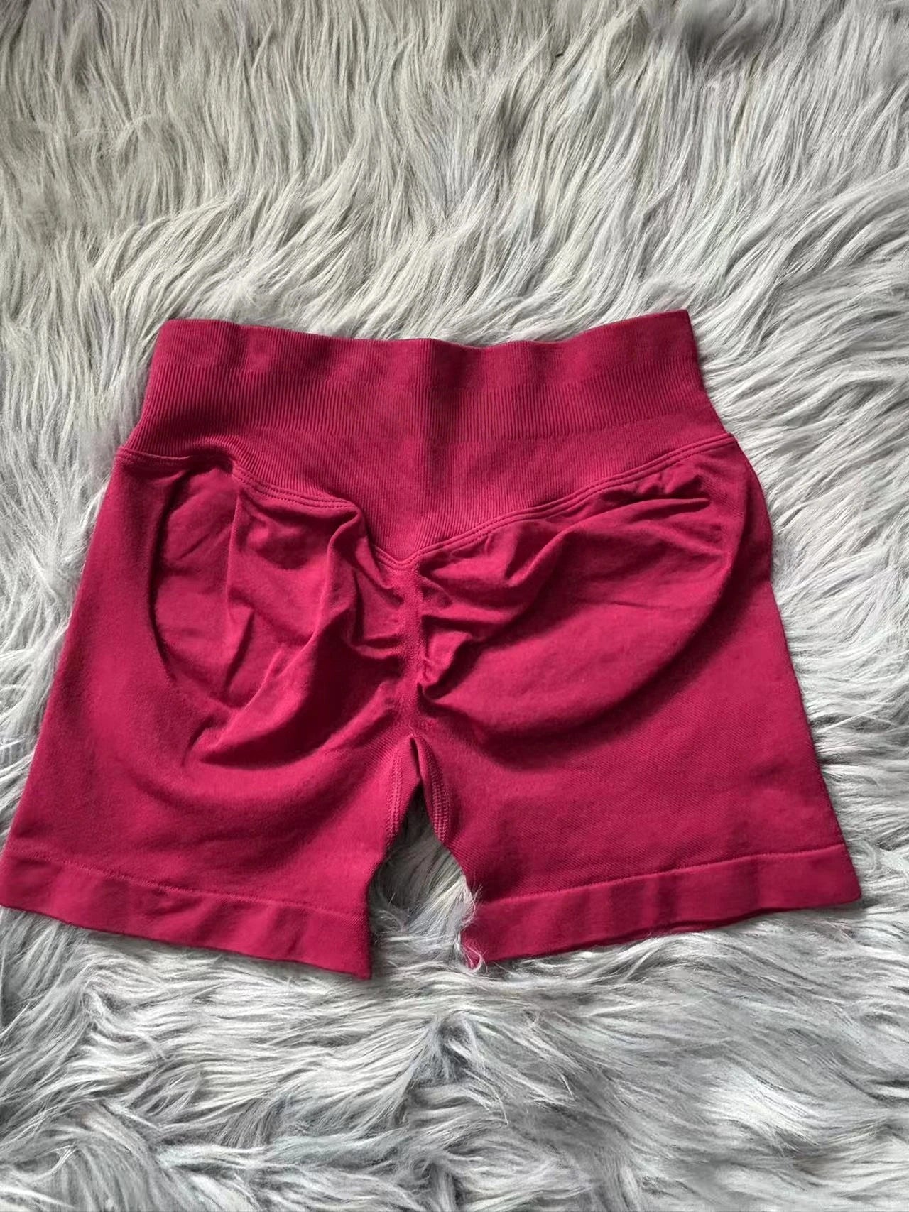 KiKis women's peach hip yoga shorts in deep pink color laid flat on a gray furry surface