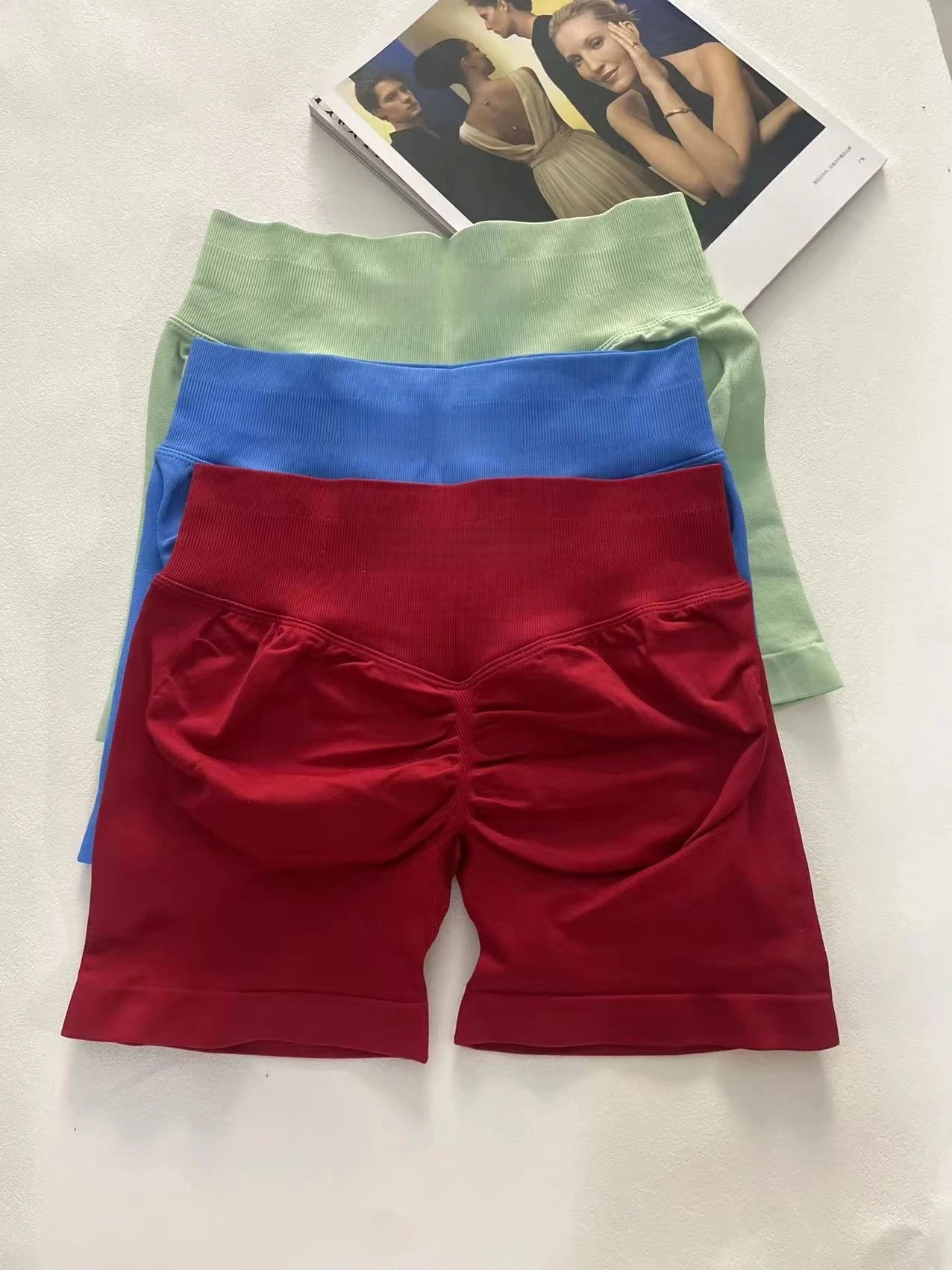 KiKis women's peach hip yoga shorts in red, blue, and green stacked on white surface