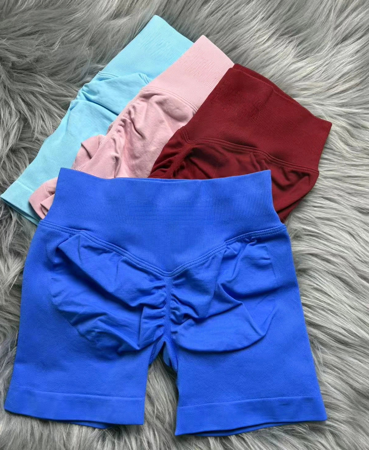 KiKis women's peach hip yoga shorts in pink with other shorts in blue, red, and light blue on gray fur background