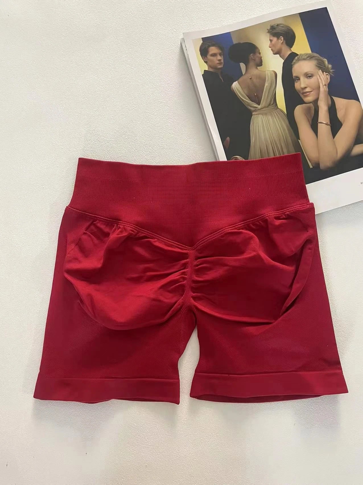 KiKis women's peach hip yoga shorts in deep red with ruched back detail laid flat on white surface