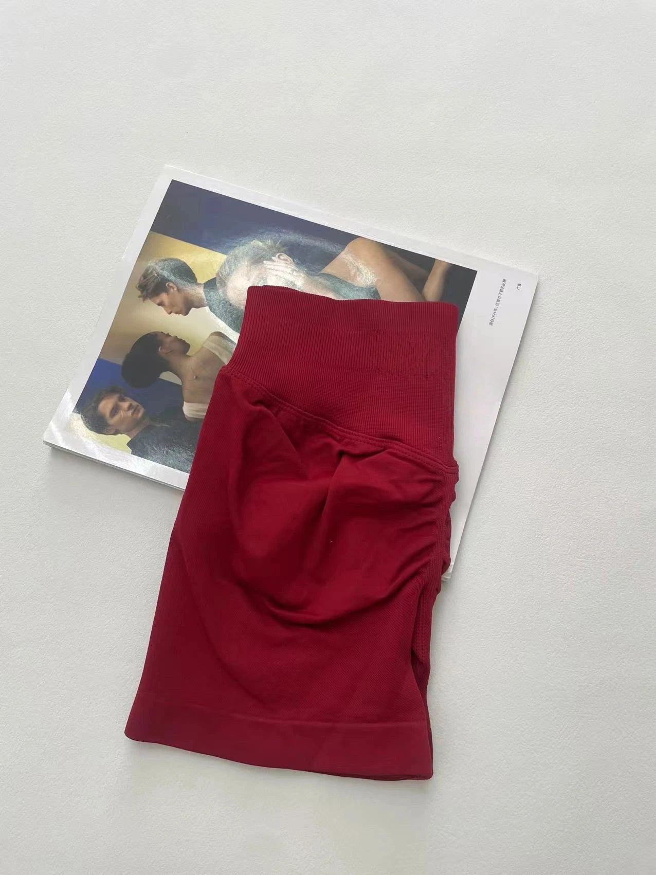 KiKis women's peach hip yoga shorts folded in deep red color on a white surface with a magazine underneath