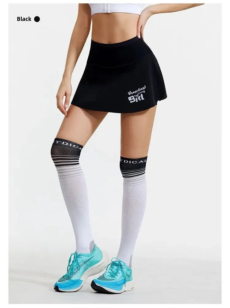 KiKis women's quick dry tennis skirt in black worn with knee-high socks and teal running shoes