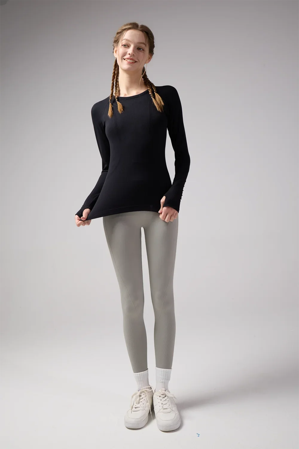 KiKis women's quick dry workout shirt in black with long sleeves worn with gray leggings and white sneakers