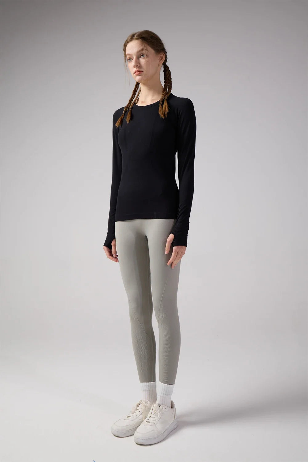 KiKis women's quick dry workout shirt in black with long sleeves worn with gray leggings and white sneakers
