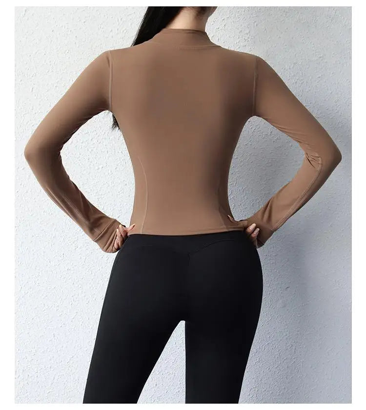 Back view of a woman wearing a brown women's slim fit yoga jacket with long sleeves and black leggings
