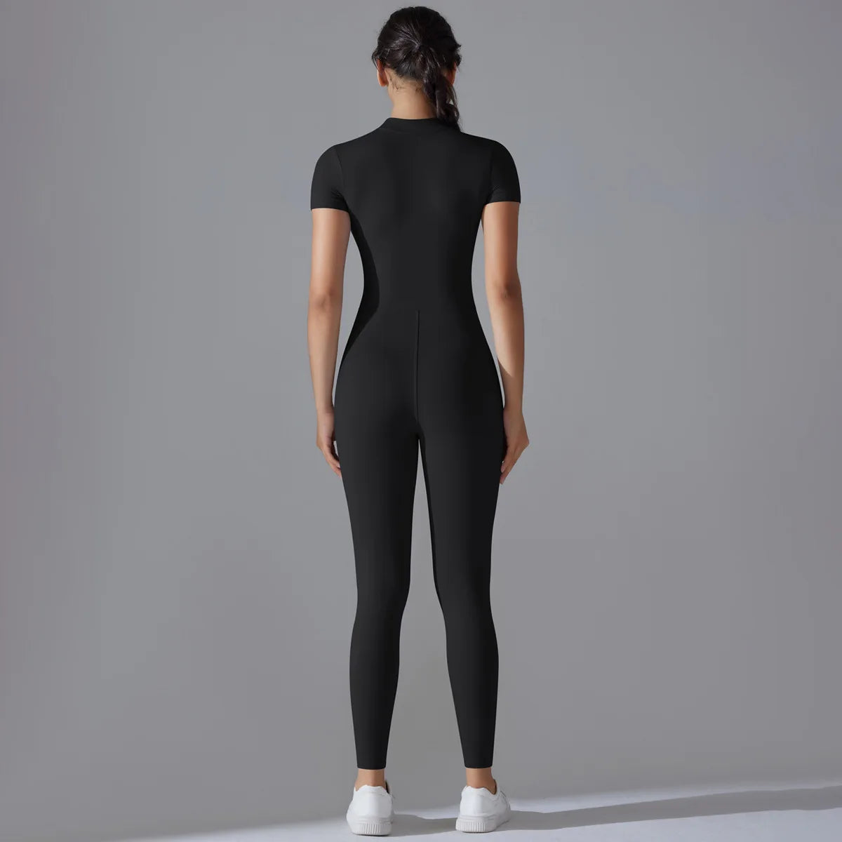 Back view of woman wearing black women's zipper yoga jumpsuit with short sleeves and white sneakers