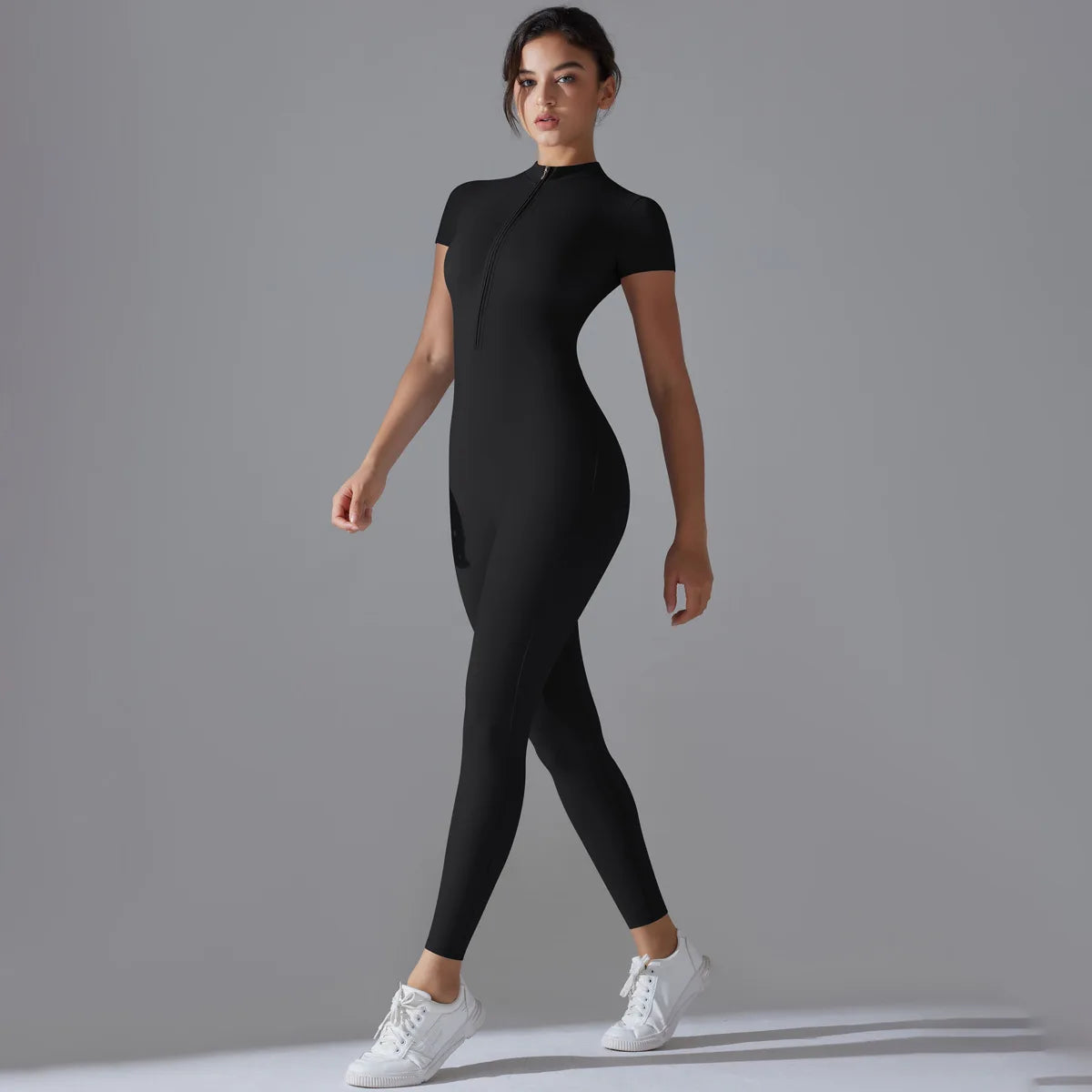 Woman wearing black women's zipper yoga jumpsuit with short sleeves and white sneakers