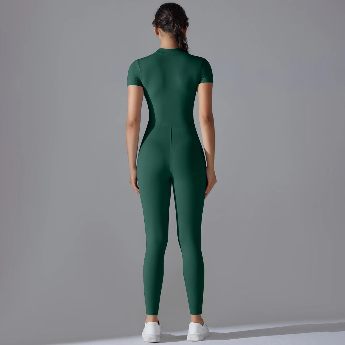 Back view of a woman wearing a green women's zipper yoga jumpsuit with short sleeves and white sneakers