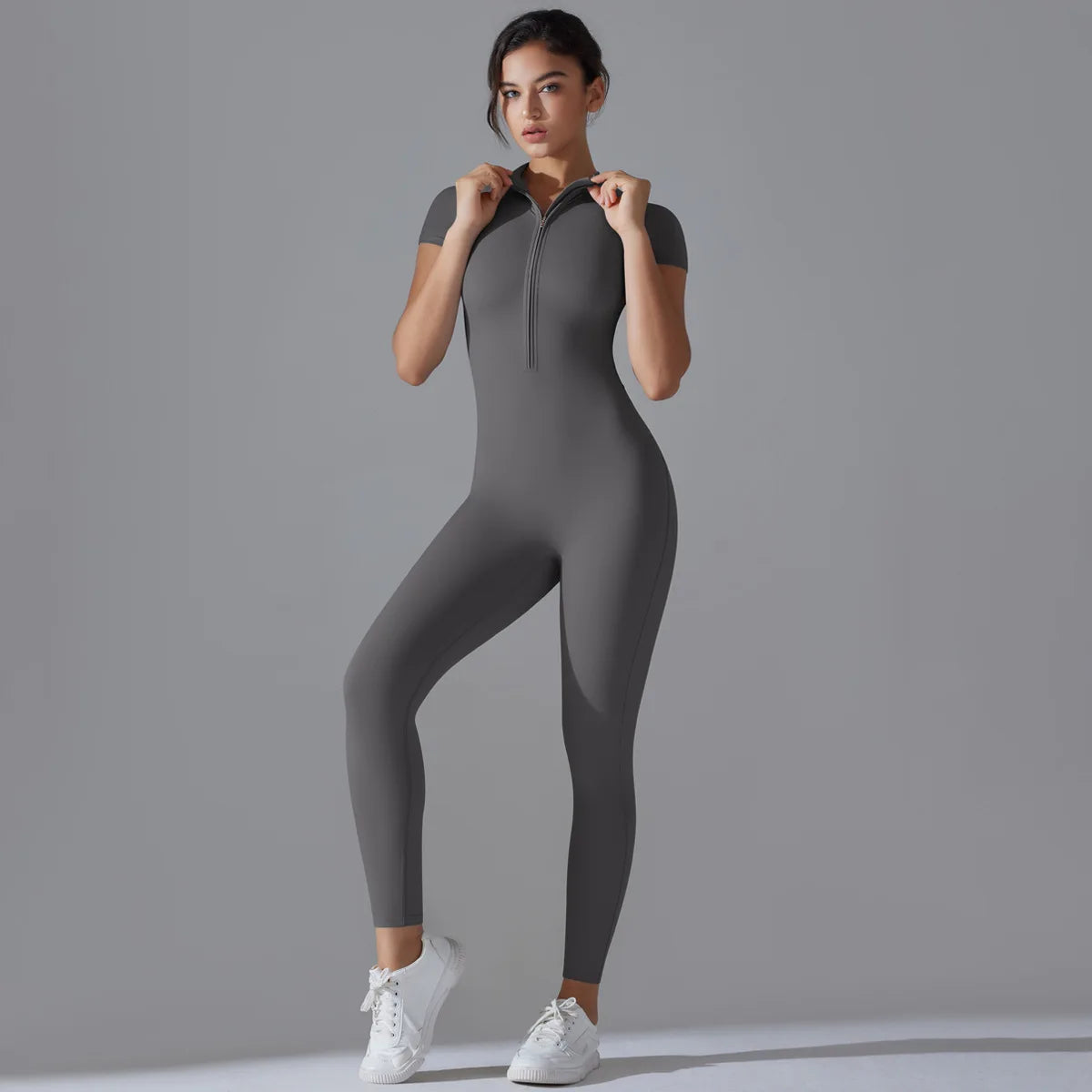 Woman wearing a gray women's zipper yoga jumpsuit with short sleeves and white sneakers