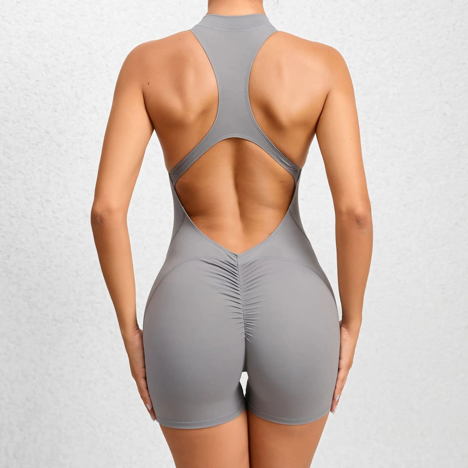 Back view of a woman wearing a gray sleeveless workout romper with open back and ruched detail