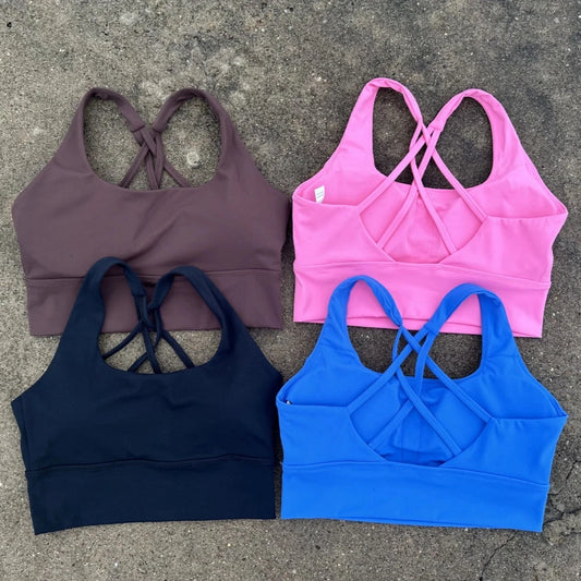 KiKis cross back sports bra for women in brown pink black and blue colors laid flat on concrete.