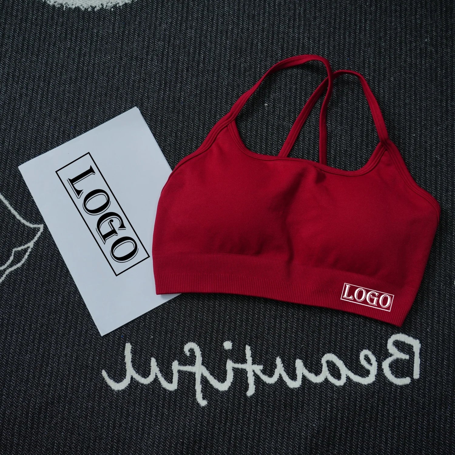 KiKis women's seamless sports bra in red with thin straps laid on a black and white textured surface