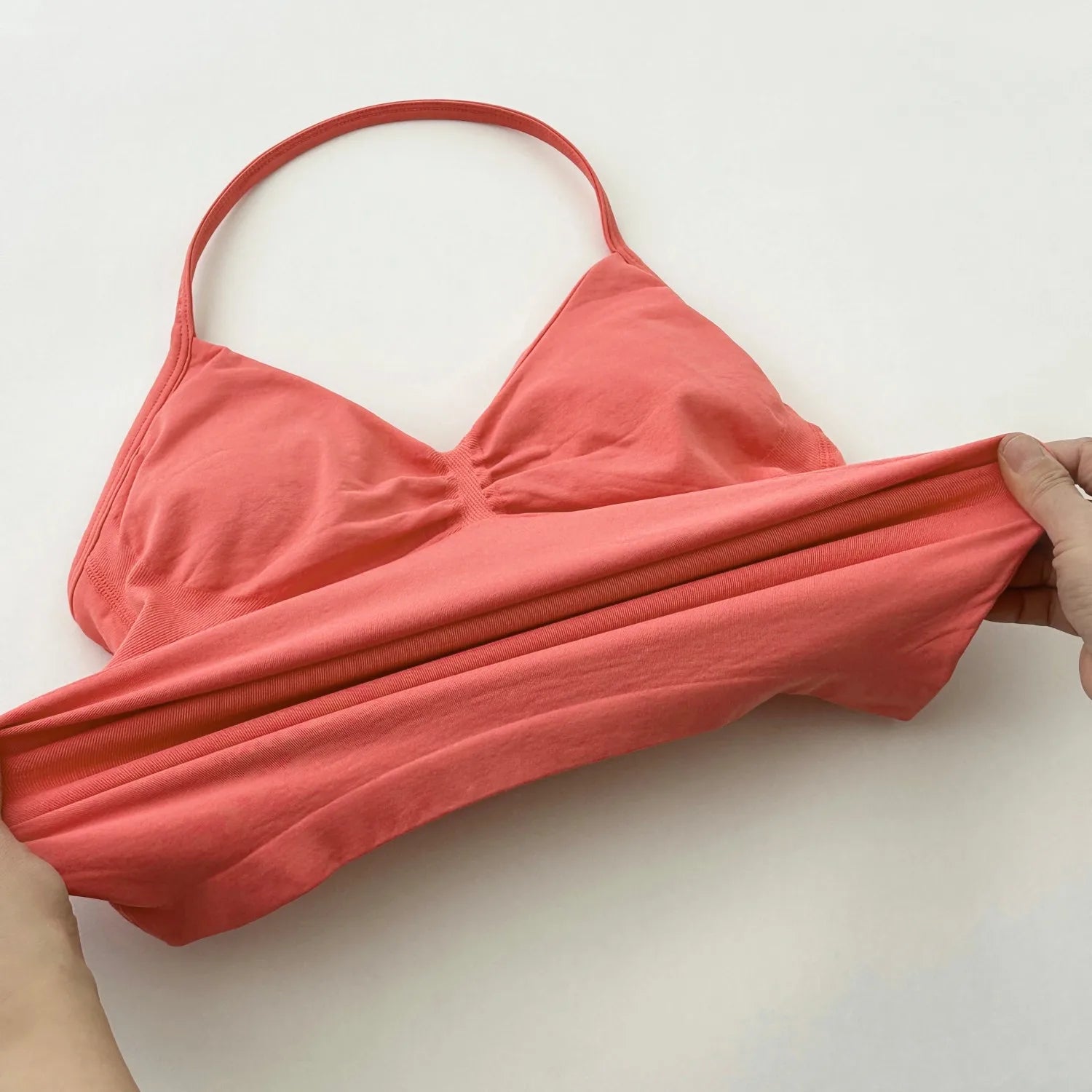 KiKis coral pink women's backless gym top made of stretchy fabric shown being stretched