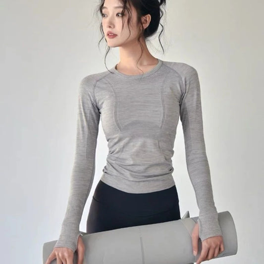 KiKis women's long sleeve yoga top in gray worn by woman holding a yoga mat